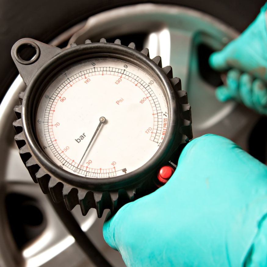 Car Tire Pressure Check in the Auto Service Garage. Checking and filling air in the tire at service station. Close-Up Of Hand holding pressure gauge for car tyre pressure measurement.