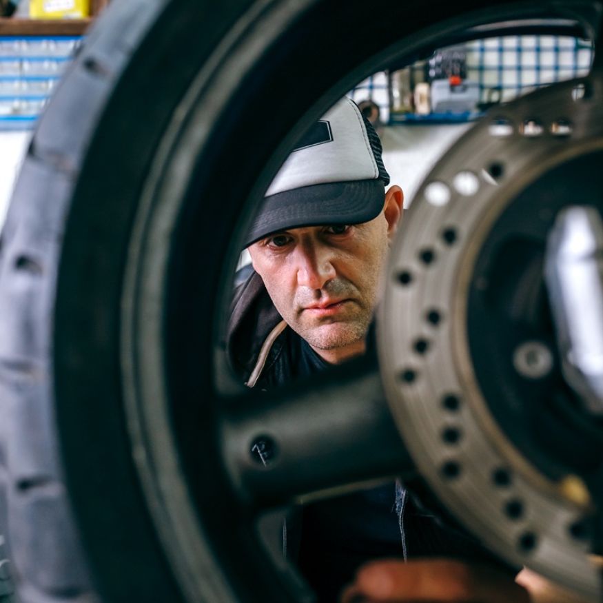 Mechanic fixing custom motorcycle wheel in his workshop. Selective focus on mechanic in background