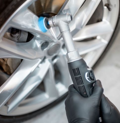 Worker in protective gloves polishing vehicle disc with professional grinder and wax from scratches, close-up